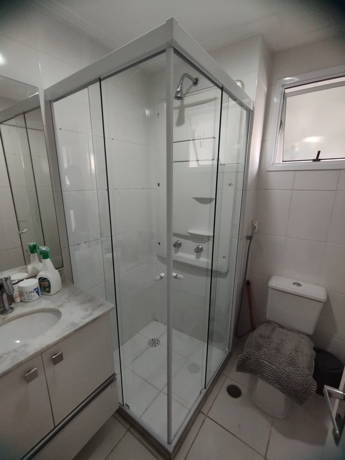 Quarto de banho com box de chuveiro de vidro, pia com pia, banheiro e janela, tudo com azulejos brancos — tex