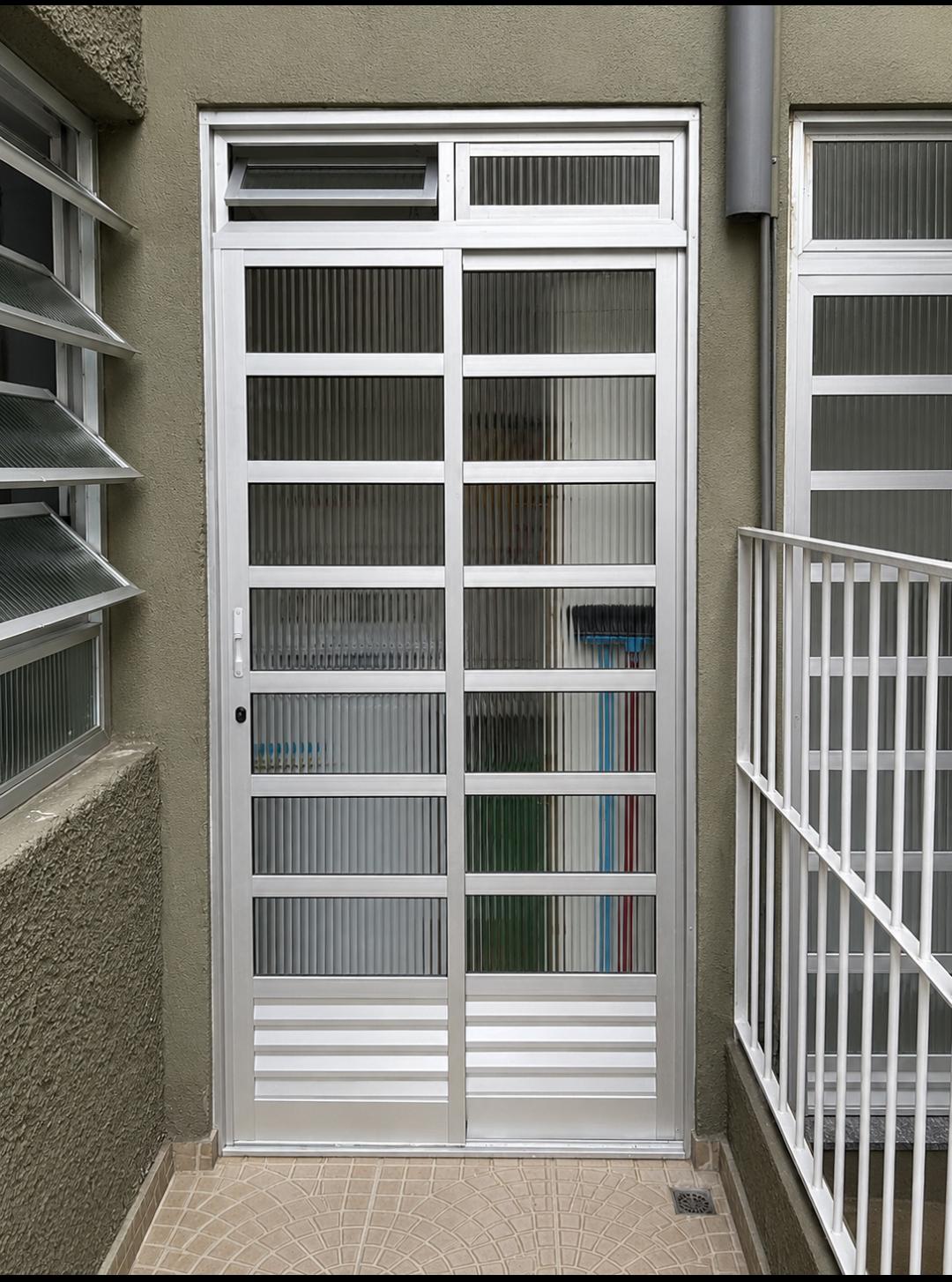 Porta de aluminio com grade de vidro em um prédio, com janelas laterais e uma escada de escorregador visível n