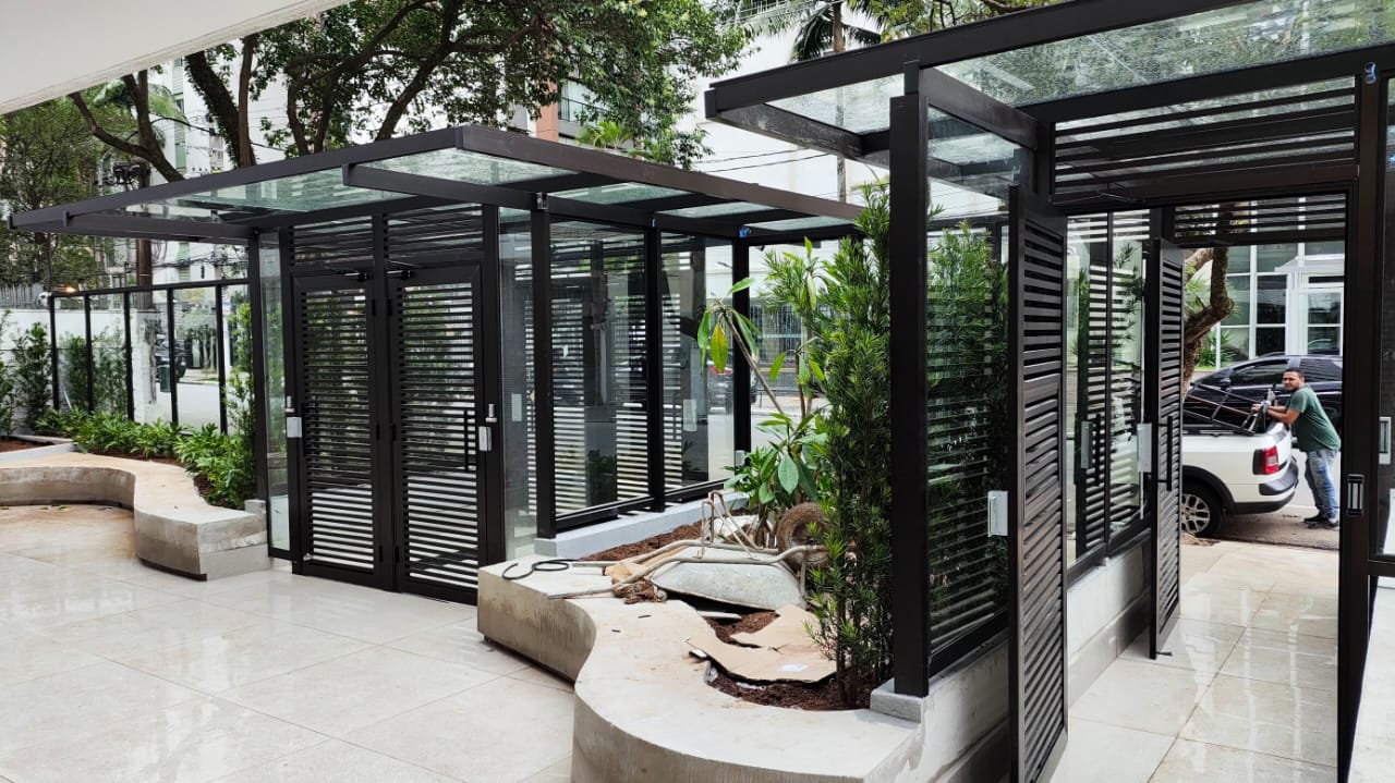 Imagem de um ambiente externo moderno com edifícios de vidro e metal, jardim e pessoas, provavelmente fachada