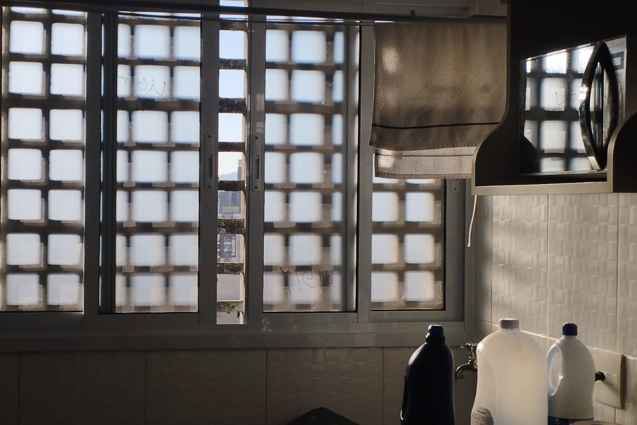 Uma janela de bloco de concreto em uma parede de azulejo, com um pano de cortina na lateral e produtos em um b