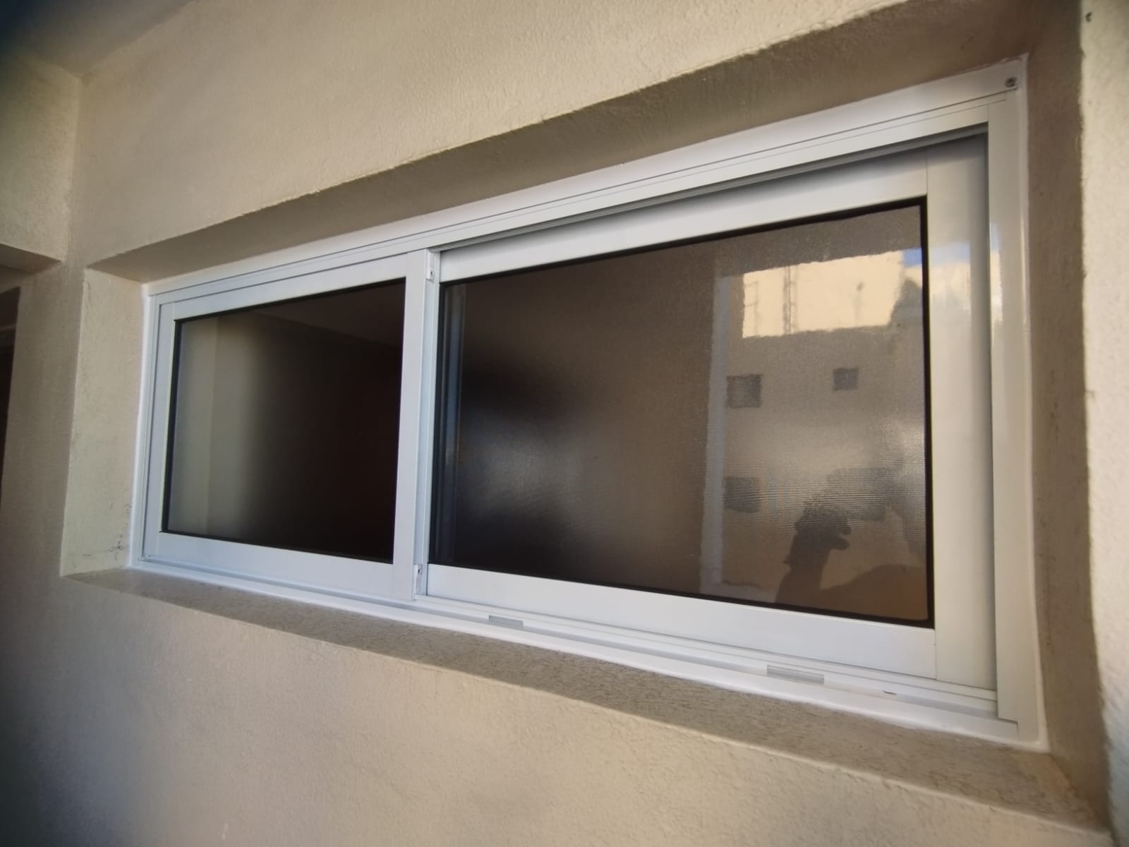 uma janela de aluminio branca com duas aberturas em uma parede de cimento