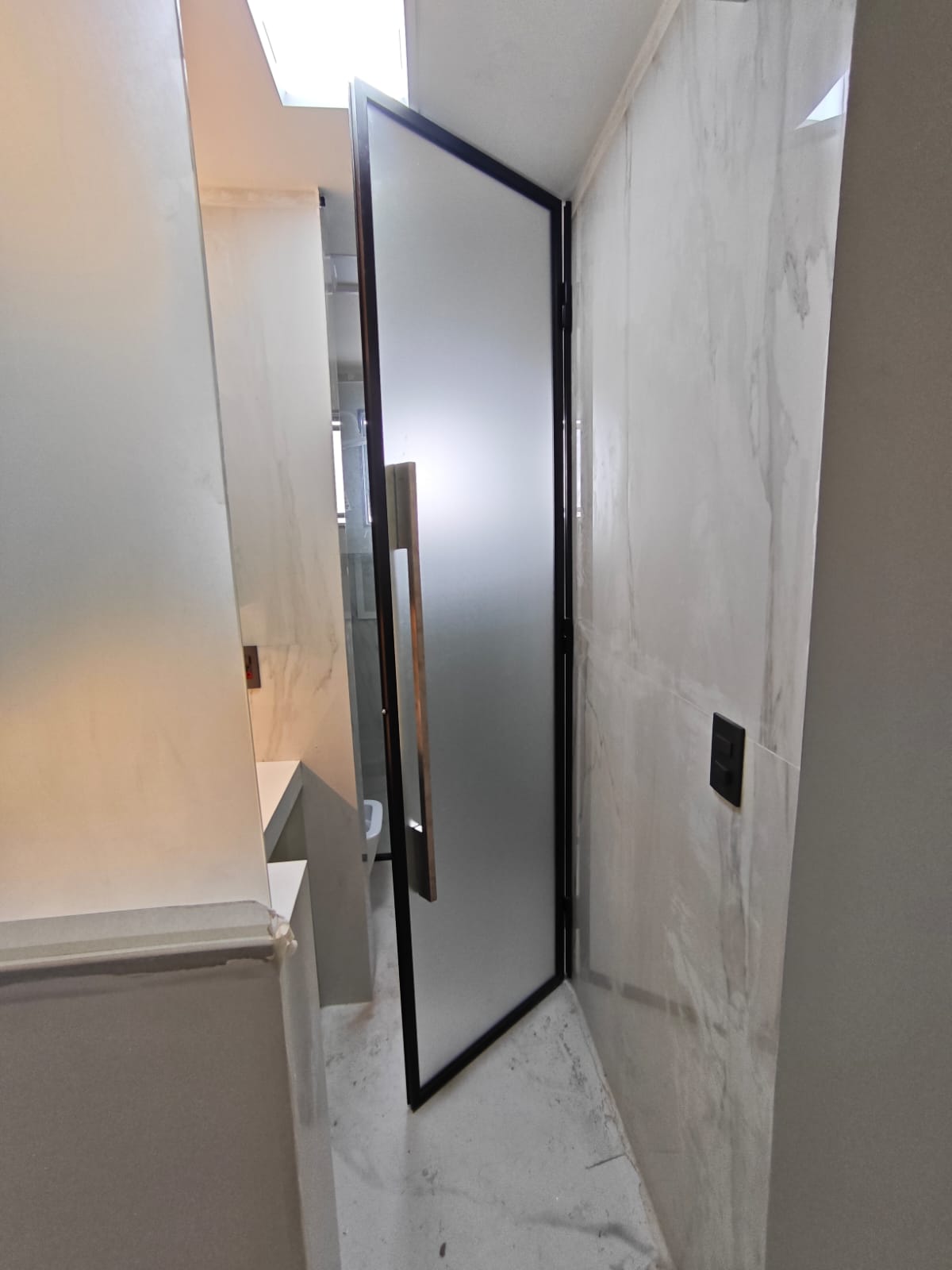 um banheiro moderno com porta de vidro fumê e paredes e piso de mármore branco